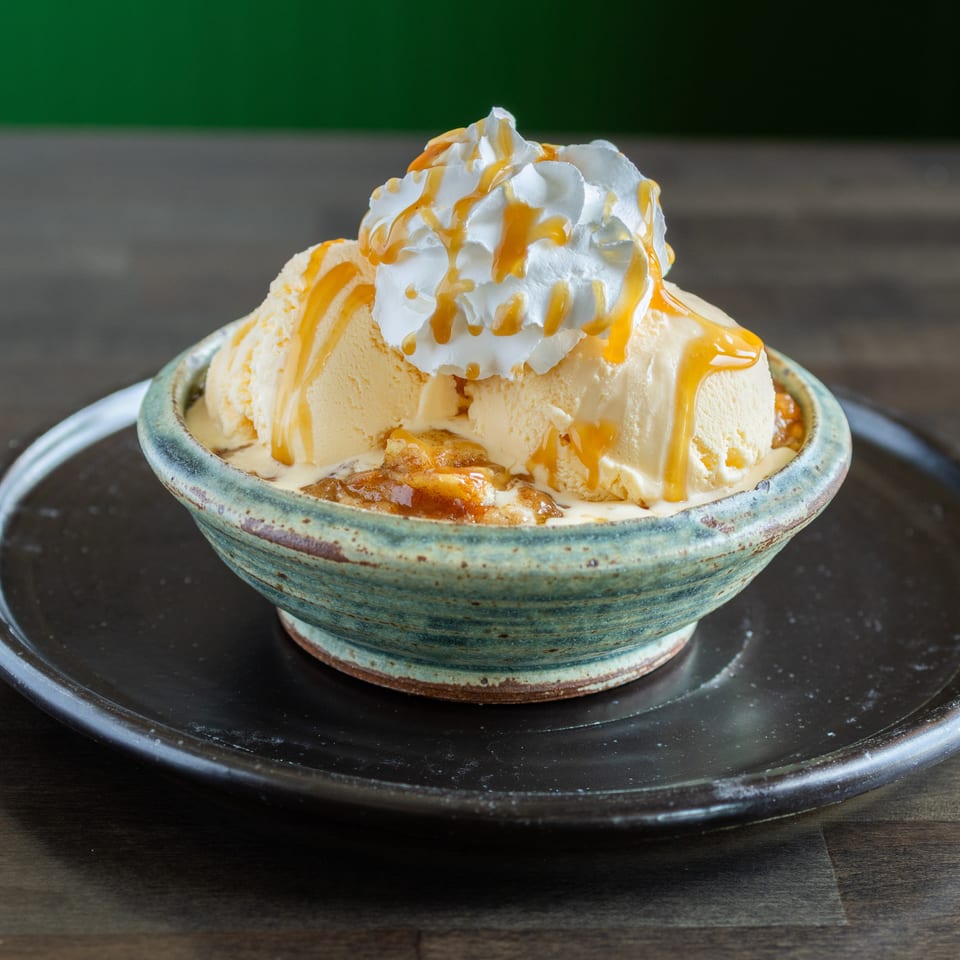 Vanilla ice cream sundae topped with whipped cream and caramel sauce in a ceramic bowl on a black plate.