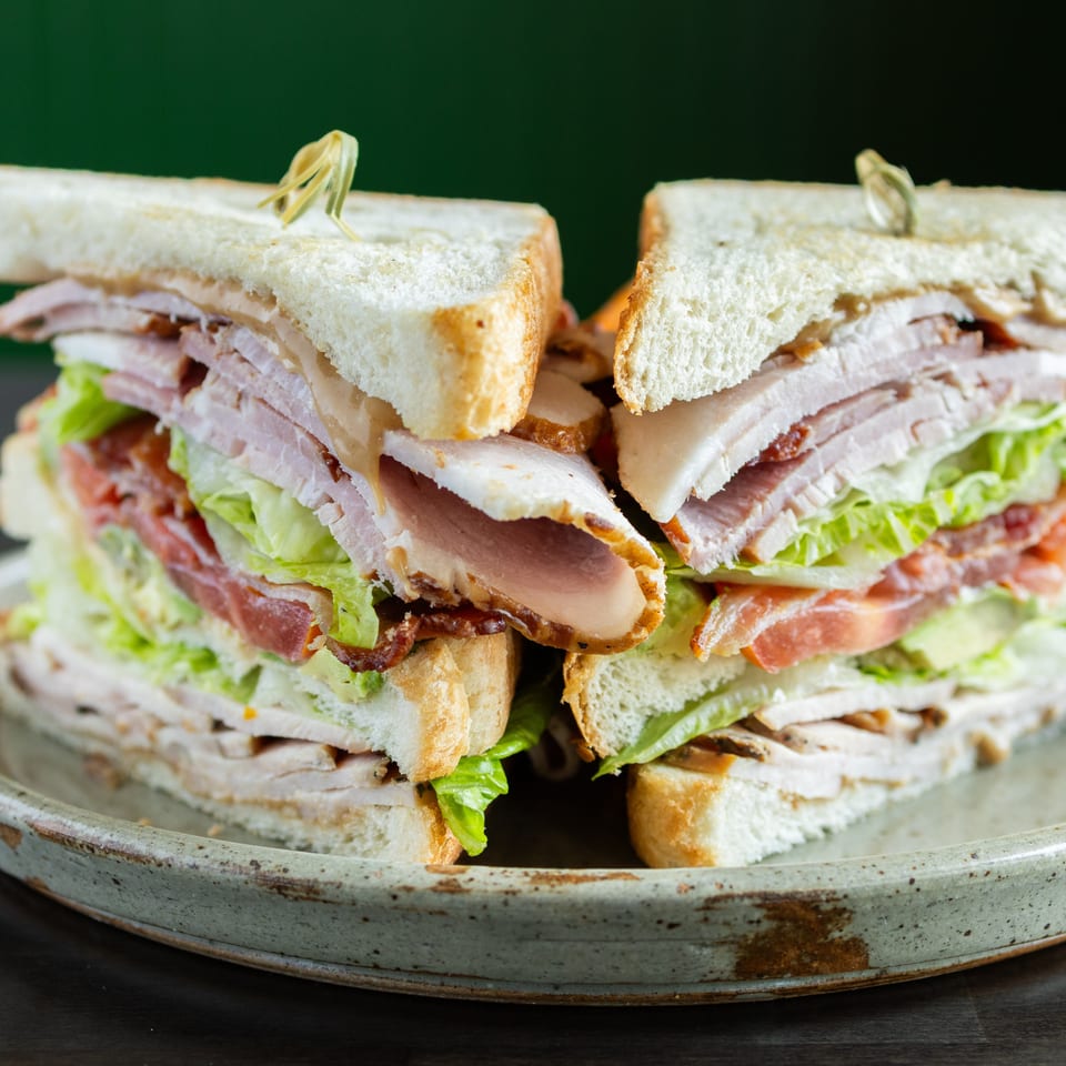 Stacked club sandwiches with turkey, bacon, lettuce, tomato, and mayonnaise on a rustic ceramic plate.