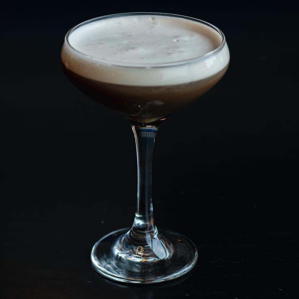 Espresso martini in a coupe glass with a thick layer of white foam on a dark surface.