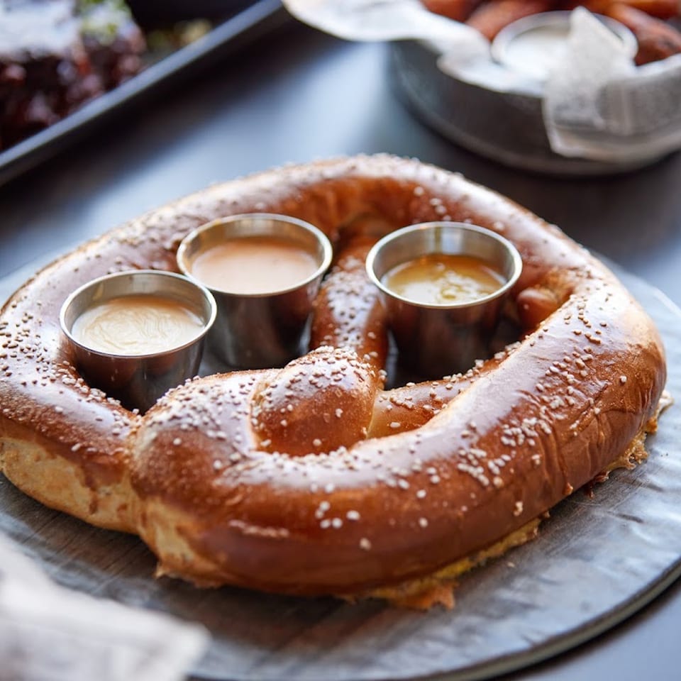 A large, salted pretzel with three dipping sauces on a round gray plate.